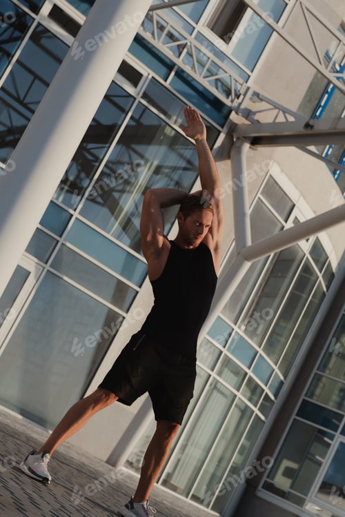 Preview: Handsome muscular man in sports clothing doing stretching exercises outdoors at early morning