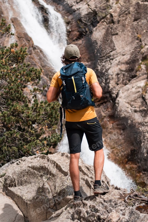 Preview: Young man with backpack observing a waterfall in Panticosa,