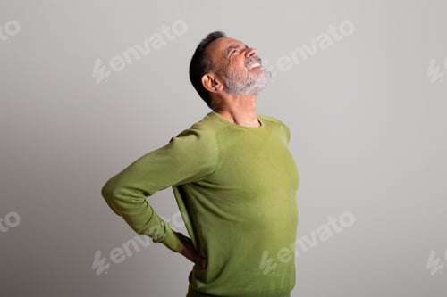 Preview: Sad caucasian elderly man in casual suffers from back pain on gray studio background