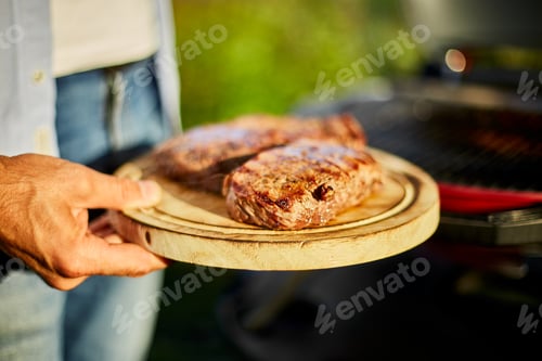 Preview: Man put down meat on a wooden board ready to eat grilled steak meat,