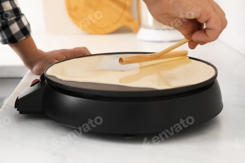 Preview: Man cooking delicious crepe on electric pancake maker in kitchen, closeup