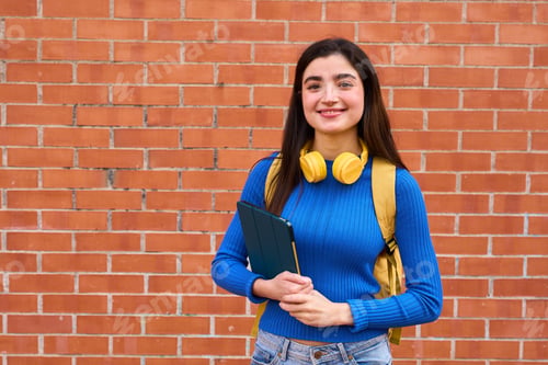 Preview: Young student with tablet standing by brick wall