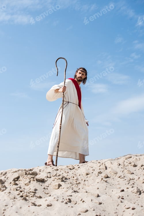 Preview: Jesus in robe, red sash and crown of thorns walking on sandy hill with staff in desert