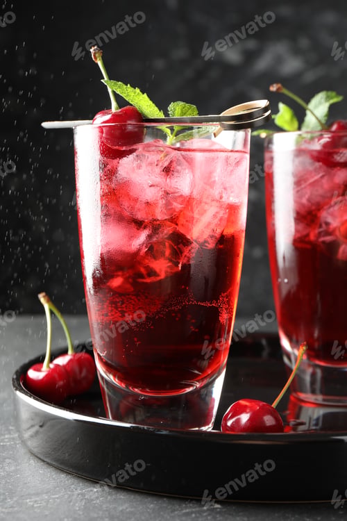 Preview: Tasty cherry soda with ice cubes, berries and mint in glasses on grey table, closeup