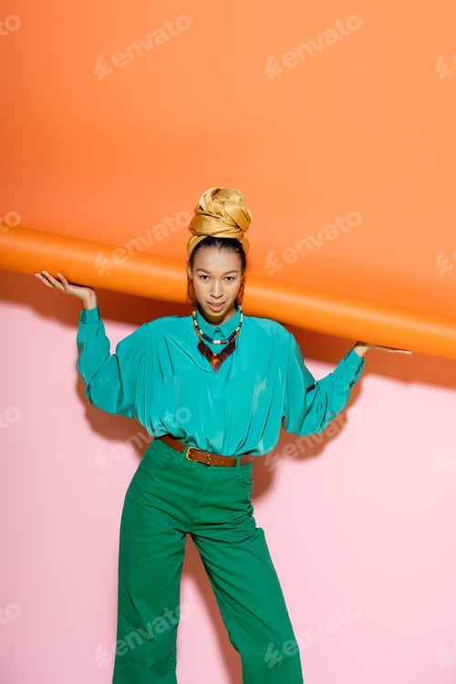 Preview: Smiling african american woman in bright outfit and headband posing on colorful background