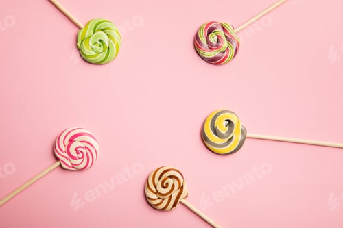Preview: top view of delicious multicolored swirl lollipops on wooden sticks on pink background