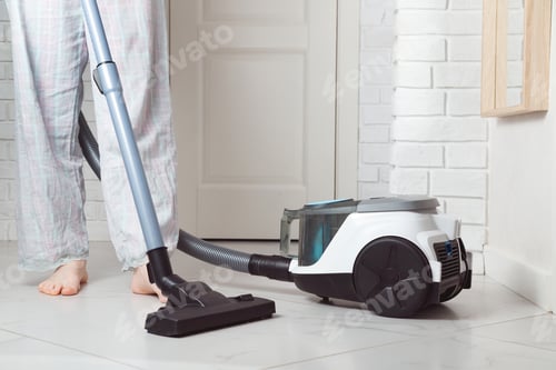 Preview: Barefoot woman cleaning ceramic tiles floor with vacuum cleaner in the modern white interior