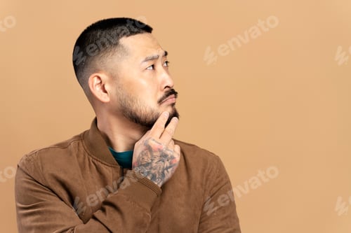 Preview: Pensive asian man touching face, choosing something, looking away, isolated on beige background