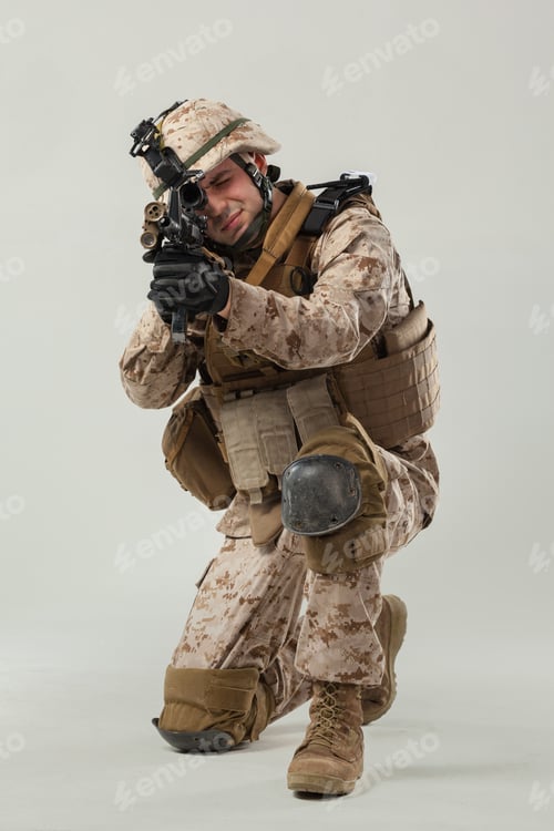 Preview: Soldier aims rifle while in a kneeling position during training exercise in military gear
