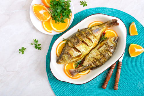 Preview: Baked roach fish with vegetables and oranges in a ceramic bowl. Top view. Diet menu