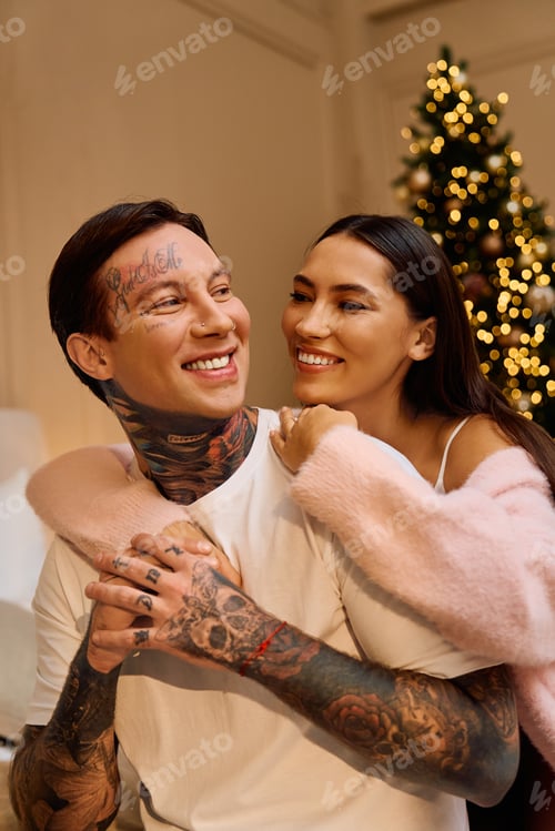 Preview: Young couple sharing joyful moments by a beautifully decorated Christmas tree