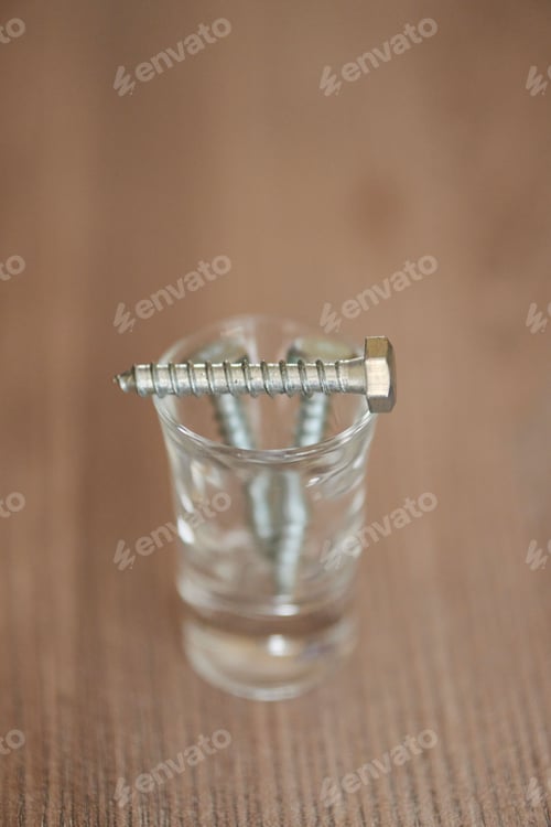 Preview: Vertical selective focus shot of a screw on a tiny glass on a wooden background