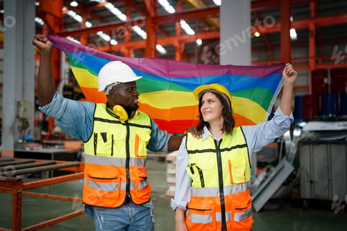 Preview: Young worker and Senior female worker holding multicolor of lgbt flag standing in factory
