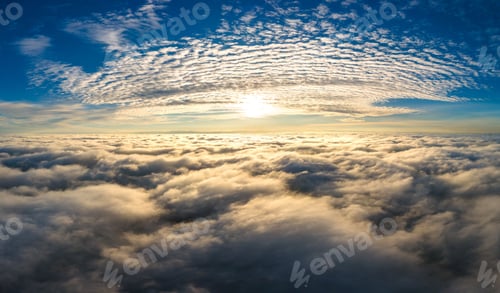 Preview: Aerial view of bright yellow sunset over white dense clouds with blue sky overhead.