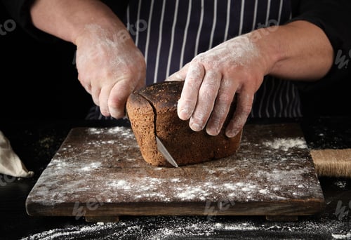 Preview: Chef in black uniform holds a kitchen knife in his hand and cuts off pieces of bread