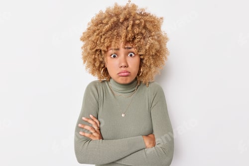 Preview: Puzzled offended woman keeps arms folded looks disappointed dressed in casual turtleneck has curly h