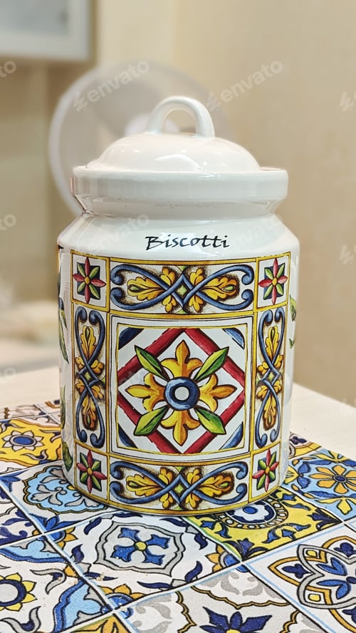 Preview: Elegant white ceramic biscotti jar with intricate colorful patterns on similarly designed cloth