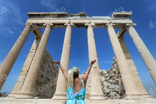 Preview: A young blonde woman raising her hands in front the ancient building of Acropolis in Athens, Greece