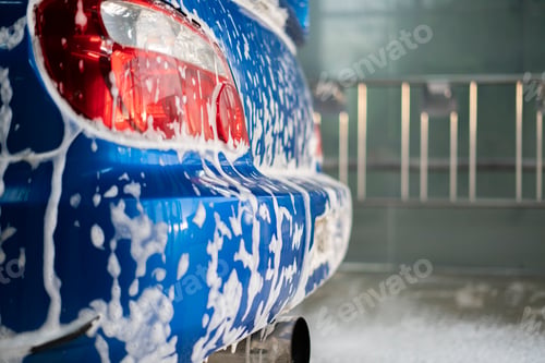 Preview: a close up blue car under the cleaning foam, inside the self washing auto service