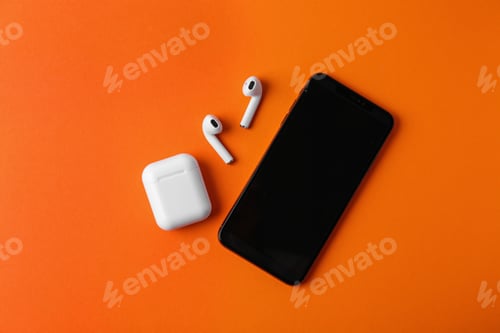 Preview: Wireless earphones, mobile phone and charging case on orange background, flat lay. Space for text