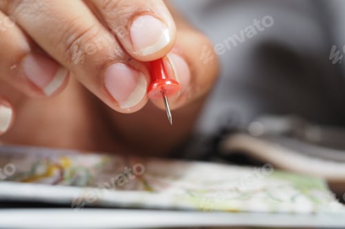 Preview: Holding a red push pin above a map on the table