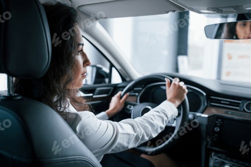 Preview: View from the inside. Beautiful businesswoman trying her new car in the automobile salon