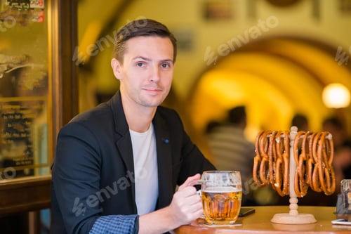 Preview: Young man with pint of beer and salted soft pretzels in beer sport bar