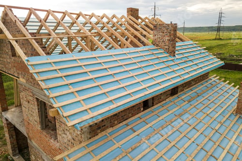 Preview: Aerial view of a brick house with wooden roof frame under construction.
