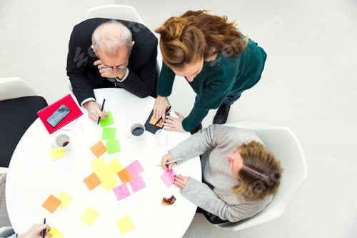 Preview: High angle view of business people with adhesive notes at table in creative office