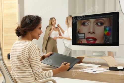 Preview: Professional African American retoucher working with graphic tablet at desk in photo studio