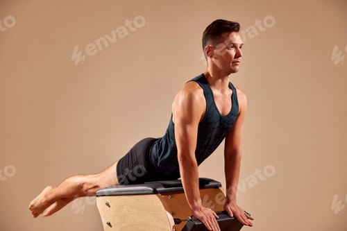 Preview: Handsome pilates male instructor performing stretching balance fitness exercise on small barrel