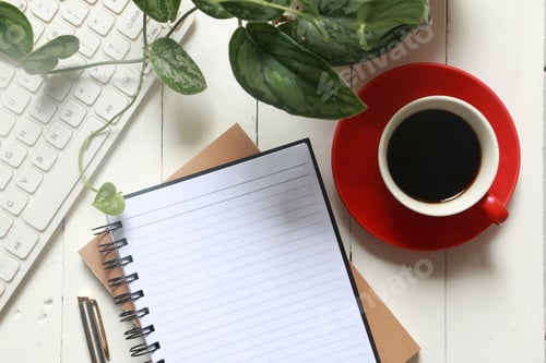 Vista previa: Plano plano de cuaderno en blanco, una taza de café, bolígrafo y teclado blanco recortado sobre una mesa de madera blanca