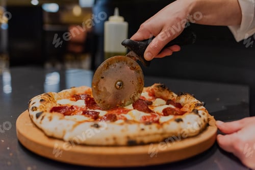 Preview: Top closeup of a hand cutting newly baked pizza with sausage and cheese on the wooden table