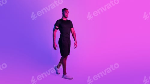 Preview: Sporty African Man With Phone Armband Walking On Purple Background