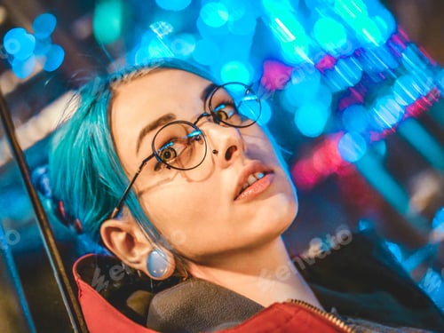 Preview: Portrait of young pretty girl with unusual hairstyle lying on glass wall which glowing colorful neon