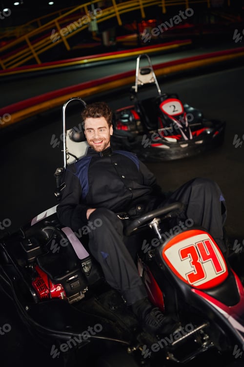 Preview: cheerful go kart driver in sportswear sitting in racing car inside of indoor circuit, winner