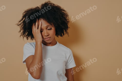Preview: Upset tired cark skinned female having headache after overwork, isolated over beige studio wall