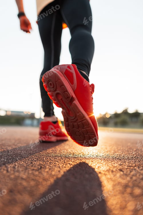 Preview: Fashionable sporty man with stylish sportswear in red sneakers walks at sunset, close-up