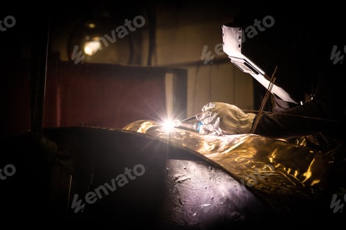Preview: Man in mask welding metal ware in darkness