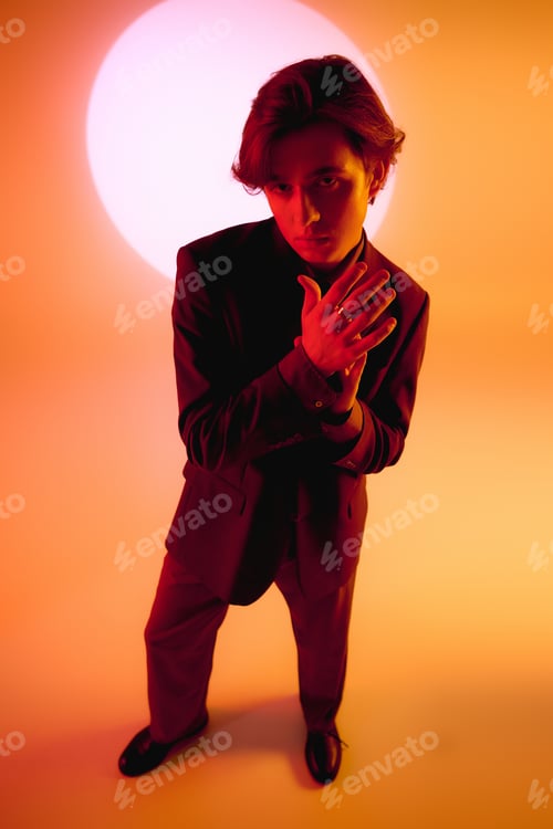 Preview: Stylish young man poses confidently against a vibrant orange backdrop at sunset