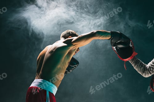 Muscular Man Boxing with Trainer in Smoky Studio