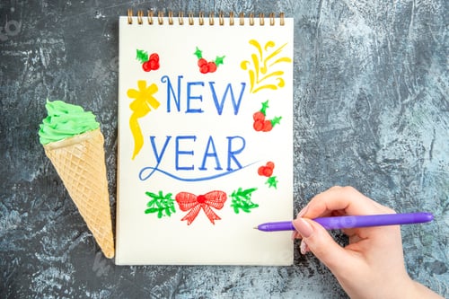 Preview: top view ice cream purple pen in woman hand new year written on notepad on grey background free