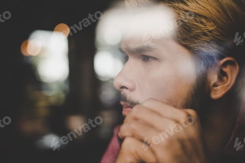 Preview: Pensive young hipster man sitting in coffee shop thinking and looking away.