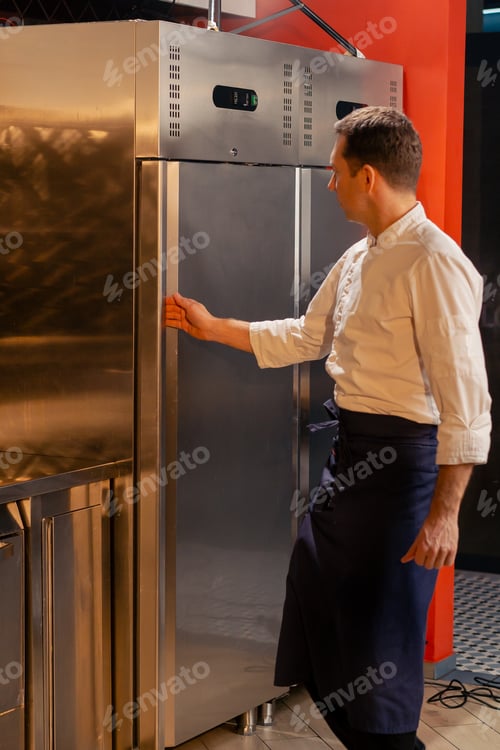 Preview: professional kitchen chef open the fridge and chooses ingredients for cooking food concept