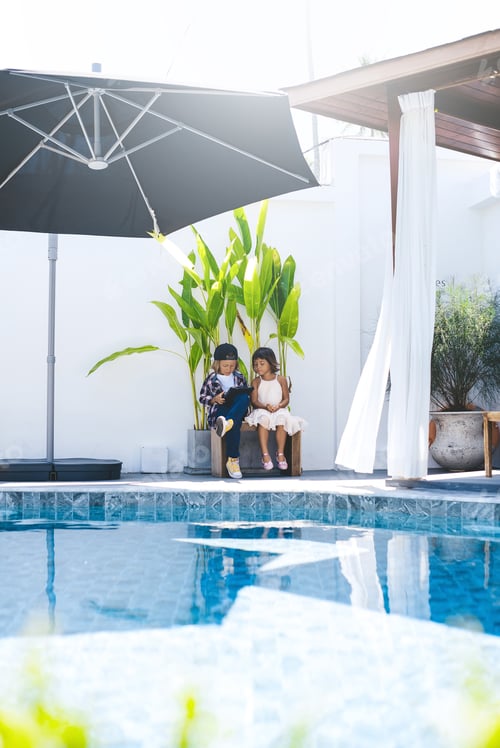 Preview: Little brother and sister sit on chair near swimming pool
