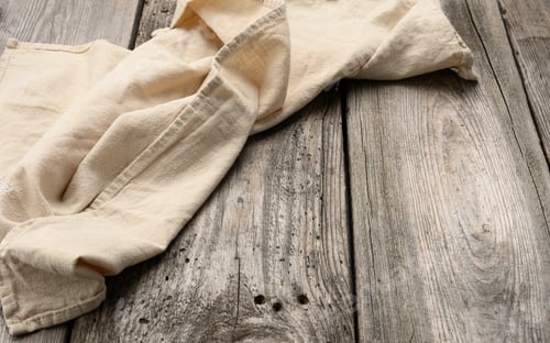 Preview: Folded beige linen towel on a table made of old gray wooden boards, top view