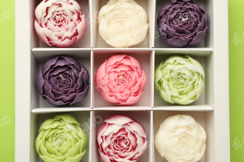 Preview: Beautiful flower-shaped candles in box on light green background, top view