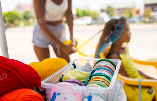 Preview: Many threads and ribbons lie on the table against the background of a girl whose African braids are