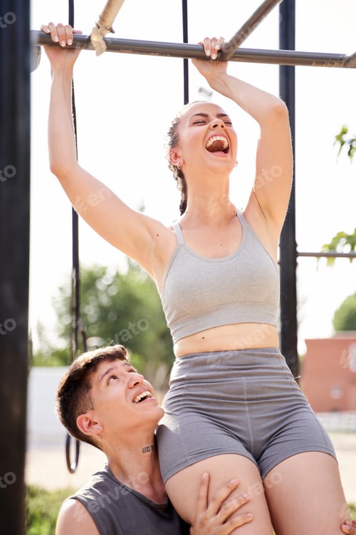 Preview: Young athletic man helps slender pretty girl to do pull up on the bar.