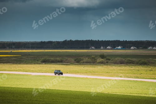 Preview: SUV Car Moving On Country Road On Background Of Green Spring Fields Or Meadow In Sunny Day
